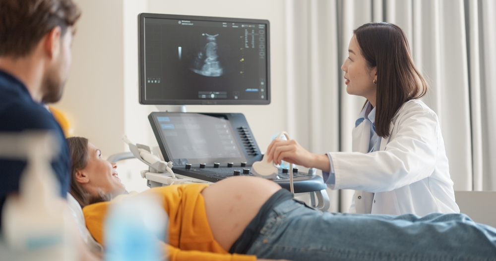 Pregnant patient receiving a prenatal ultrasound as a clinician uses the transducer with the monitor visible nearby.