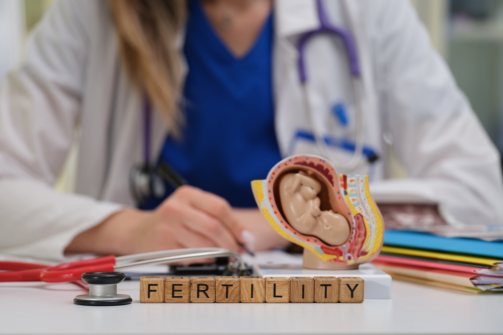 Healthcare professional with stethoscope at a desk, fertility uterus model and wooden blocks spelling FERTILITY.