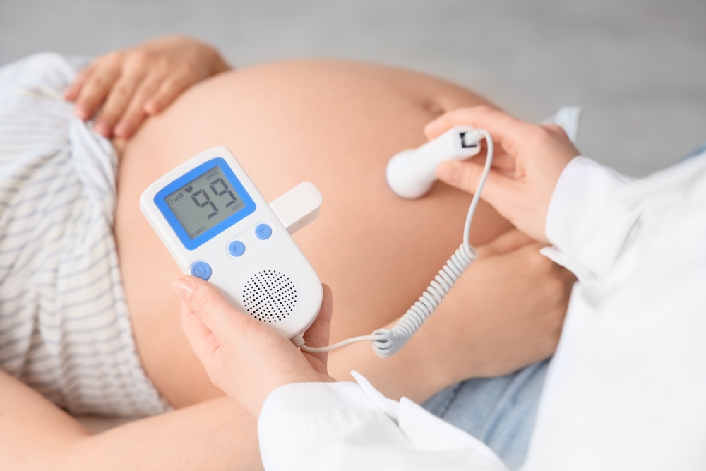 Pregnant belly with a handheld fetal Doppler on the abdomen showing 95 bpm on the display.
