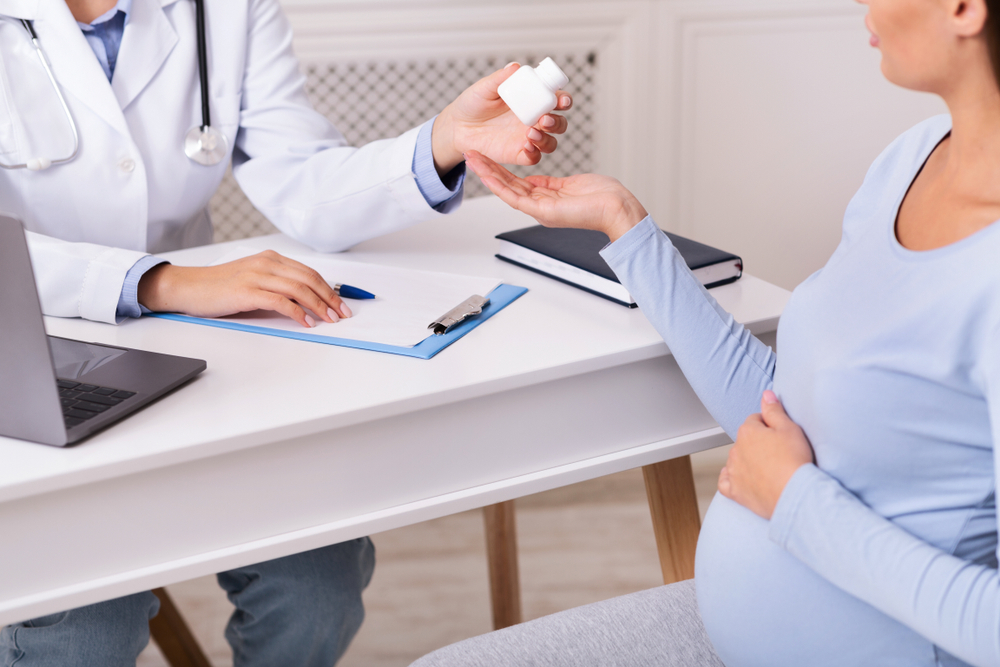 Doctor giving a pill to a pregnant patient during a clinic visit, seated at a desk with medical documents nearby