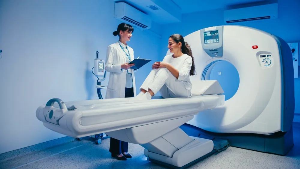 MRI Medical imaging room with a patient seated on a CT scanner table as a clinician reviews notes, preparing for a scan