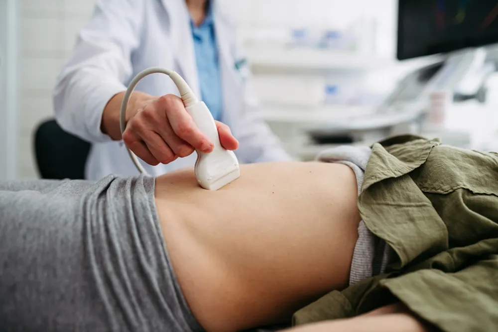 Ultrasound Medical professional performs an abdominal ultrasound, placing a handheld transducer on a patient’s bare midsection.